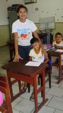 Foto mostra professora com aluno surdo na sala de aula.