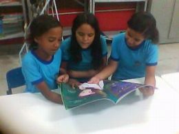 Três alunos leem livro na biblioteca