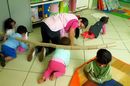 Professora e alunos engatinham no chão da sala de aula