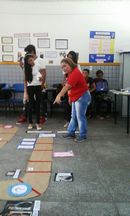 Professora e alunos observam trilha de jogo no chão da sala